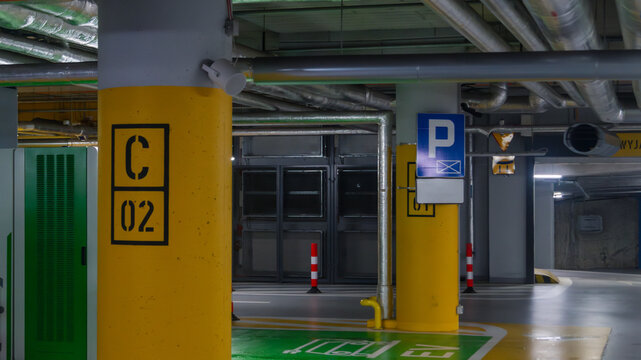 Underground parking with yellow and green coating. Underground parking with a pile of pipes on the ceiling and a parking sign
