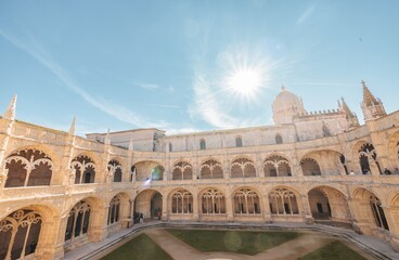 Fototapeta premium Visitors wander through the stunning courtyard of Jeronimos Monastery, marveling at the intricate stonework and enjoying the warm sun above as they soak in Portugal's rich culture