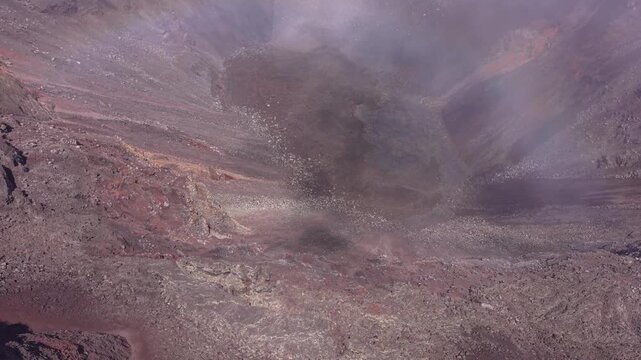 Drone footage ascending above a volcanic crater at Piton de la Fournaise Reunion Island.Fog moves across the scene,revealing and obscuring sections of the crater while the camera slowly gains altitude
