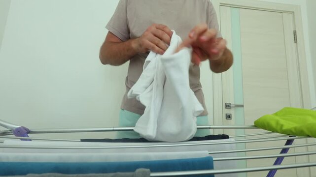 A man demonstrates a quick, efficient method for folding white t-shirts on a drying rack in a clean, minimalist home environment.
