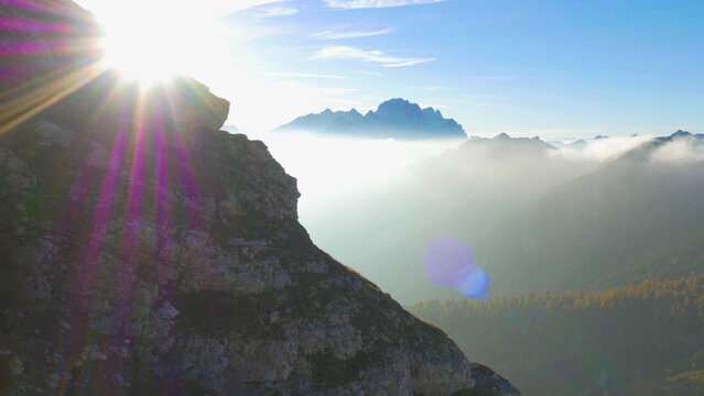 LENS FLARE: Flying close to a rocky hill of a high mountain in the sunny Alps. - Powered by Adobe