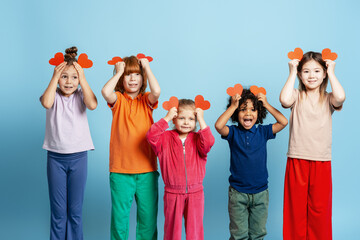 Diverse happy children holding red heart shapes over their heads, expressing love