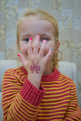 little girl covered her face with her hand, young girl covers her face with her hand and has a manicure and butterfly painted on her arm