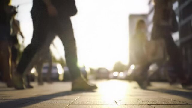 Low angle video of diverse pedestrians in casual clothes, legs in focus, walking on a vibrant, sun-drenched urban street with golden hour flare and creamy bokeh. Dynamic urban energy