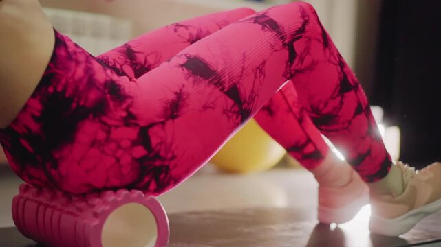 woman on foam roller activating ankles and feet, pink leggings and light sneakers, gentle plantar flexion and heel lifts, sunlit studio floor, gradual transition from recovery to dynamic movement,