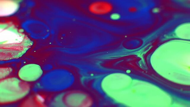Mesmerizing macro video of iridescent blue, red, and green viscous liquid paint swirling, merging, and flowing into intricate, organic cell patterns with soft backlighting. Concept of abstract fluid