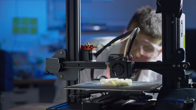 Professional engineer observes the 3D printing process in a modern laboratory while adjusting the equipment and recording data.