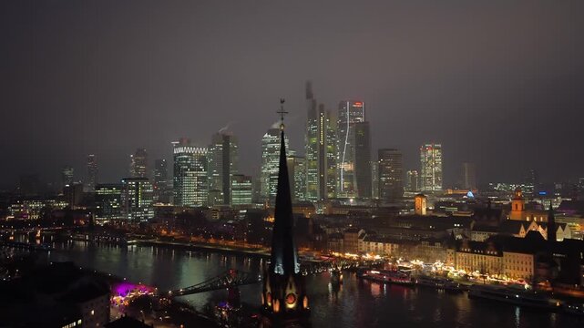 Aerial view of illuminated Frankfurt financial district on a foggy night. Modern skyscrapers and traditional buildings reflect on Main River