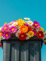 Vibrant flowers overflowing from a trash can against a clear blue sky, viewed from a low angle with image focus on the colorful blooms
