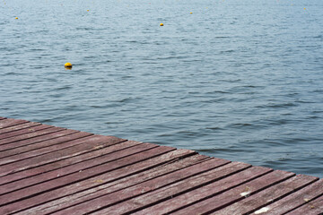 Wooden pier over calm water surface with yellow floating buoys. Minimalist seascape or lakeside background with copy space. Concept of summer, vacation, travel, tranquility, nature and relaxation.