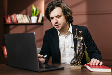 Businessman working on a laptop at a desk with a Lady Justice statue, bookshelves, and a potted plant in a modern office. Concept business, office work, professional environment © wedmoments.stock
