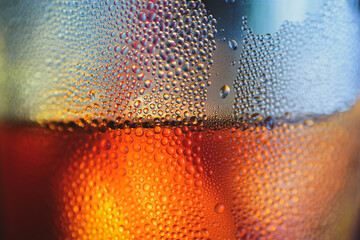 Macro shot of a glass of amber-colored beverage, covered in droplets. The image showcases the condensation forming on the surface, with a blurred background. 