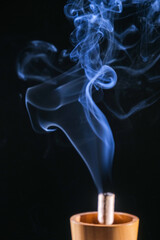 Abstract blue smoke emanating from a wooden incense holder, curling gently upwards against a black background