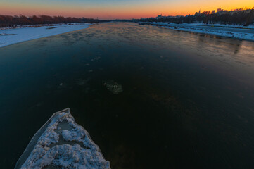 Widok z Mostu Gdańskiego na rzekę Wisłępo kt&oacute;rej płynie  kra lodowa o zachodzie słońca.