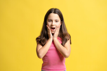 Portrait of amazed little girl with open mouth looking at camera isolated on yellow background