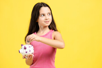 Beautiful girl holding piggy bank throwing coins looking away on copy space on yellow background