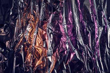Crumpled metallic foil texture with purple and orange neon light reflections