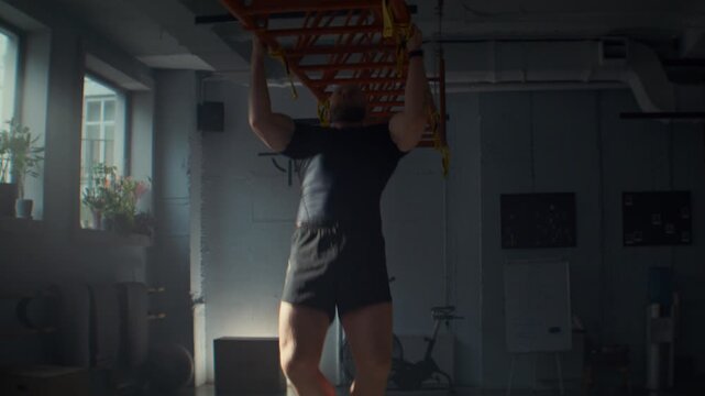 Strong man in black activewear does pull ups on metal beam in gym