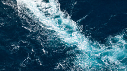 Obraz premium High-angle aerial close-up of a white foaming wake created by a vessel on the surface of the deep blue sea.