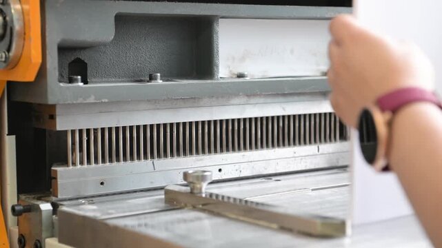 Women's hands in the printing house work at the machine, making holes in the paper to insert the spring for the notebook. Production of calendars and brochures