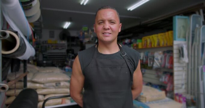 Smiling Hispanic small business hardware store owner standing inside shop expressing confidence pride resilience independence hands on leadership local entrepreneurship