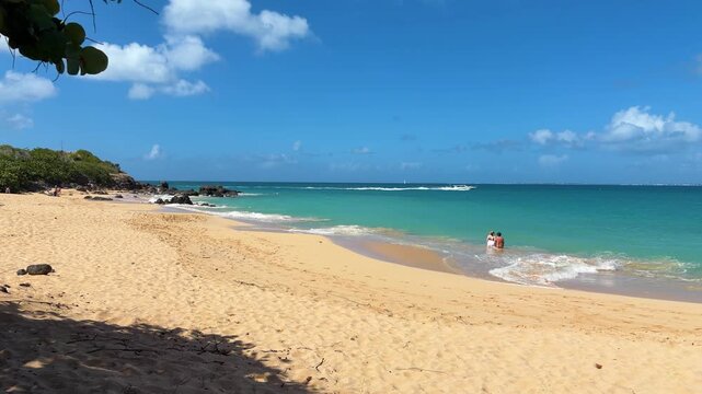 Golden sandy beach, the bright blue and turquoise waters of the Caribbean Sea and and people swimming in shallow water on the island of St. Maarten. Saint Martin is an island in the Caribbean.