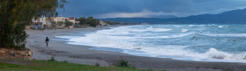 Stormy beach coastline with lone person walking by rough sea