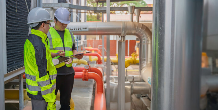 Two Asian engineers inspecting industrial cooling system valves. Professional technicians use a digital tablet for maintenance checks of thermal control equipment at a manufacturing plant.