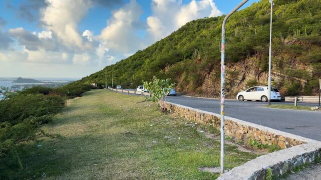 Saint Martin Island, view from the observation deck of the Caribbean Sea, a green mountainside, and cars passing along the highway on a clear sunny day. Saint Martin is an island in the Caribbean.