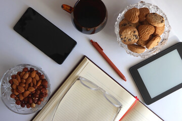 Notebook, pen, tablet, phone, coffee and snacks on white background. Top view. 