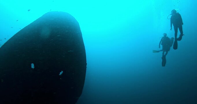 Group of scuba divers explores a massive shipwreck in deep blue water, surrounded by bubbles and soft light rays. Cinematic slow motion underwater adventure and discovery.
