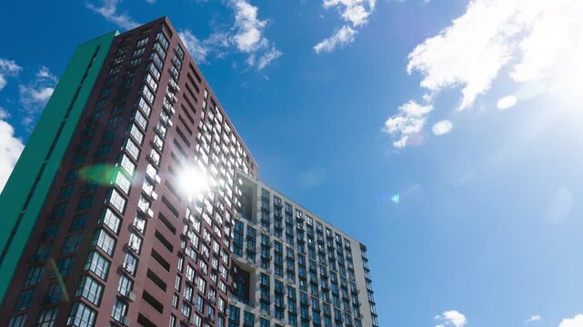 Low angle view of modern apartment building against blue sky. Timelapse of white clouds moving fast over high-rise residential tower in the city