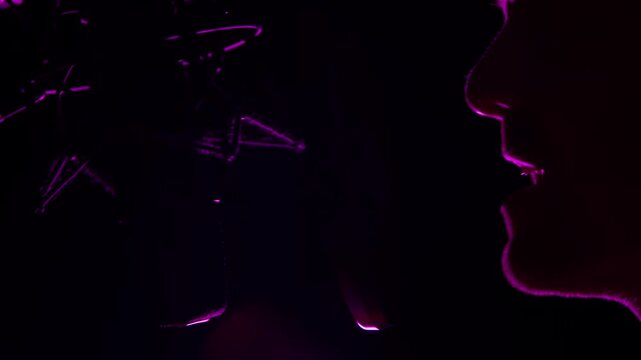 Silhouette of a Male Singer Recording Artist at a Studio Microphone. A male singer, rapper, or recording artist is seen in silhouette at the microphone of a darkly lit recording studio.