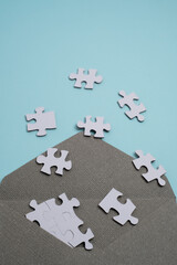 Fototapeta premium White jigsaw puzzle pieces falling out of a craft paper envelope on blue background. Problem solving and logic concept.