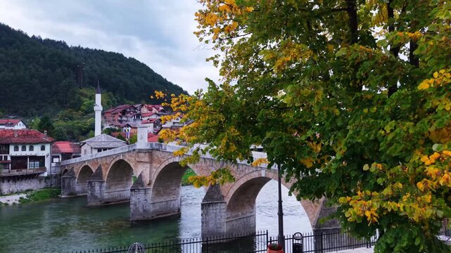 Cinematic view of historic stone bridge framed by autmn tree leaves