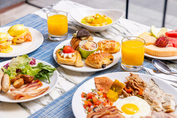 Gourmet breakfast spread with eggs benedict, pastries, fresh fruit, orange juice, and assorted meats on marble table, perfect for brunch or hotel dining.