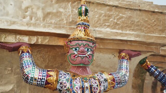 Close up of a colorful demonic Yaksha guardian statue holding up a golden stupa at Wat Phra Kaew, famous landmark in Bangkok, Thailand