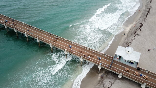 Aerial view of the Juno Beach Pier extends into the turquoise ocean where white waves crash onto the sandy shore, Juno Beach, Florida, United States.