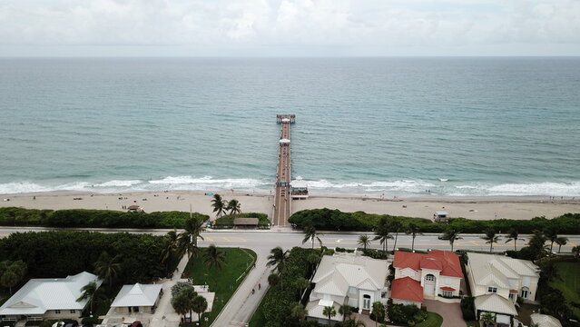 Aerial view of the Juno Beach Pier stretches out to the ocean, contrasting with the nearby houses and lush greenery, Juno Beach, Florida, United States.
