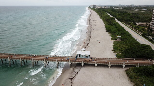 Aerial view of the Juno Beach Pier stretching out into the turquoise Atlantic, the shore lined with lush green vegetation, a beautiful contrast of natural colors, Juno Beach, Florida, United States.