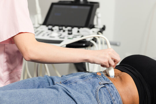Ultrasound transducer is scanning lower abdomen above jeans on exam table with portable machine