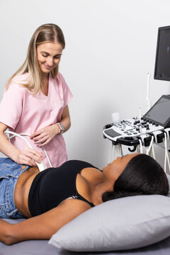 Female clinician and African American patient having abdominal ultrasound using probe at clinic