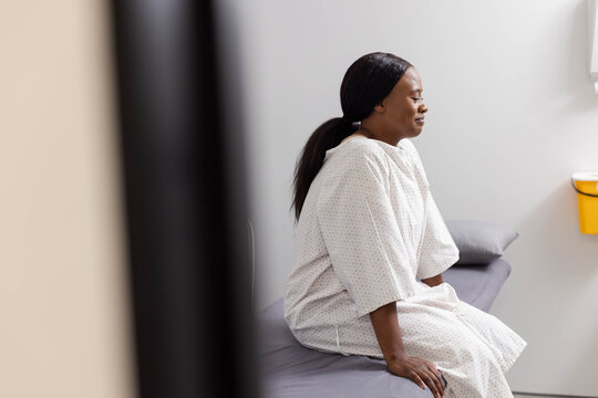 Woman sitting on exam couch in clinic wearing light gown beside yellow container