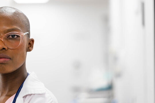 Adult African American woman standing in clinic, wearing lab coat, stethoscope, glasses, copy space