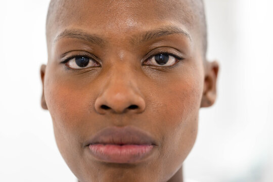 Woman with shaved head holding direct gaze, posing in studio with white backdrop and soft lighting