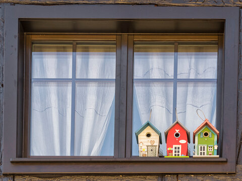 ventana con bonitos visillos y tres casitas para p&aacute;jaros decoradas con forma de casas coloridas