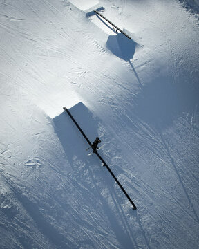 Aerial view of snow-covered landscape with metal rails casting long shadows in the stark sunlight, Avoriaz, Auvergne-Rhone-Alpes, France.