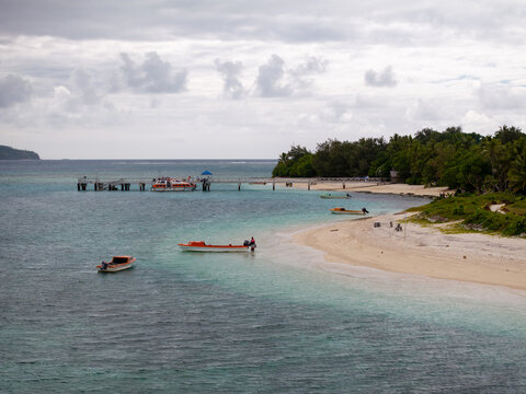 Aerial view of the tranquil beach meeting the turquoise sea, with a pier reaching out into the water under a cloudy sky, Mystery Island, Vanuatu.