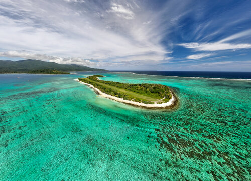 Aerial view of a tropical island surrounded by turquoise waters and coral reefs under a sky streaked with wispy clouds, Mystery Island, Vanuatu.