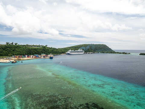 Aerial view of turquoise waters meet the deep blue harbor where a cruise ship docks near vibrant shipping containers, Port Vila, Shefa Province, Vanuatu.